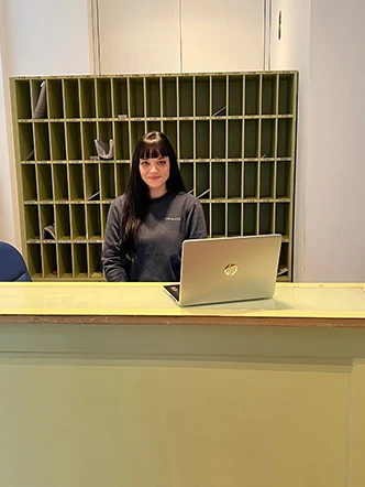 Recepcionista atendiendo en el mostrador, con el casillero de correspondencia al fondo